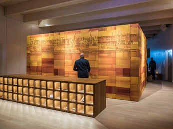 Holzvertäfelter Raum mit historischer Schrift an der Wand, Besucher betrachtet die Ausstellung.