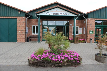 Eingang des Informationszentrums "Tor zum Moor" mit Blumenbeet im Vordergrund und Backsteinfassade.