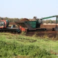 Ein Torflader und ein Bagger arbeiten in einem weiten Moorgebiet unter klarem Himmel, umgeben von Vegetation.