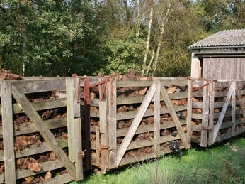 Ein Stapel von hölzernen Moorkarren voller Torf steht an einem Schuppen im Grünen, umgeben von Bäumen.