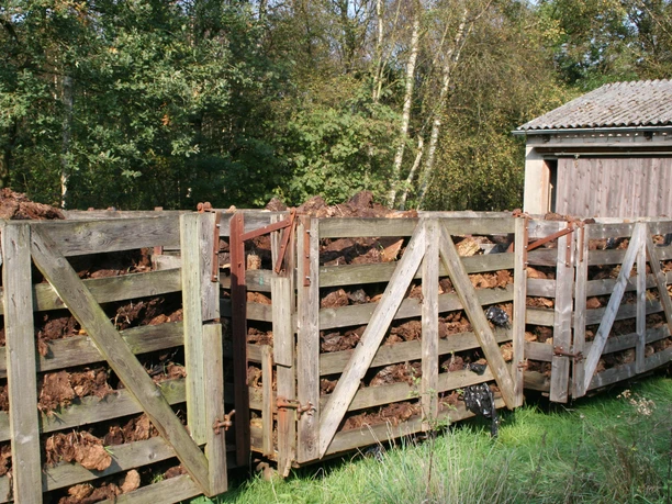 Moorbahn Ein Stapel von hölzernen Moorkarren voller Torf steht an einem Schuppen im Grünen, umgeben von Bäumen.