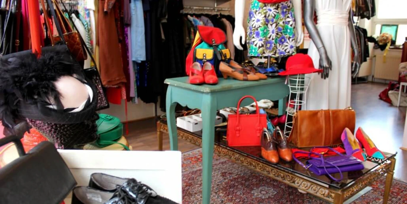 Polyestershock Ein detailreiches Vintage-Geschäft präsentiert farbenfrohe Kleidung und stilvolle Accessoires auf Tischen.A detailed vintage store presents colorful clothing and stylish accessories on tables.