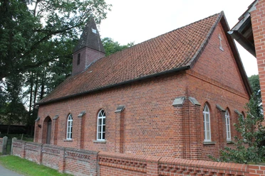 Rote Backsteinkapelle mit spitzem Turm, umgeben von Bäumen, Teil des Dorfes Wendenborstel.