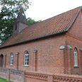Rote Backsteinkapelle mit spitzem Turm, umgeben von Bäumen, Teil des Dorfes Wendenborstel.