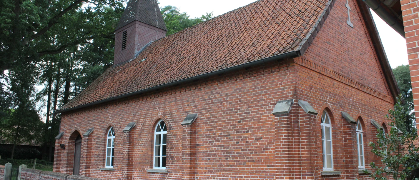 Rote Backsteinkapelle mit spitzem Turm, umgeben von Bäumen, Teil des Dorfes Wendenborstel.