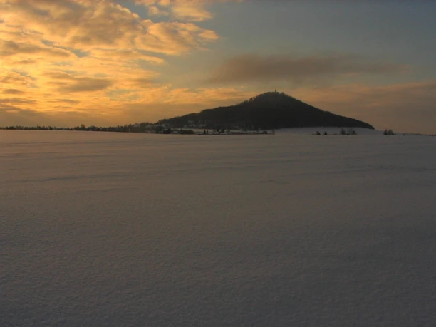 Snow-covered hill in the evening light against a cloudy sky, quiet winter landscape.