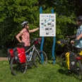 Radeln an der Bifurkation - Klaus Herzmann.JPG Zwei Radfahrer betrachten eine Infotafel an einem sonnigen Tag im Grünen.
