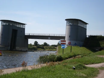 Zwei Türme flankieren das Intscheder Wehr über einem Fluss, umgeben von grüner Vegetation.