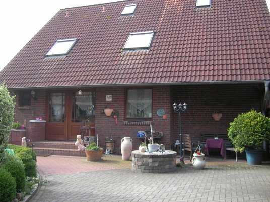 Ein rotes Backsteinhaus mit Satteldach, bepflanztem Vorgarten und dekorativen Terrakottatöpfen.