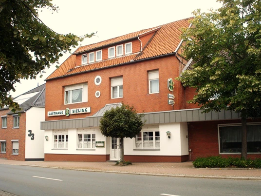 Das Hotel Sieling präsentiert eine rote Backsteinfassade mit klassischem Satteldach und grüner Beschilderung.