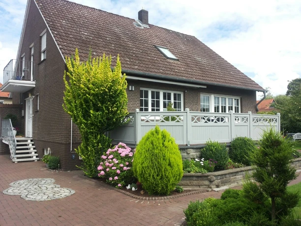 FeWo Kropp Großzügiges Backsteinhaus mit gepflegtem Garten, dekorativen Pflanzen und hellem Zaun.