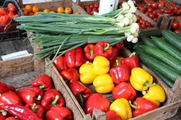 Bunte Paprika, Gurken und Lauchzwiebeln liegen in rustikalen Holzkisten auf einem Marktstand.