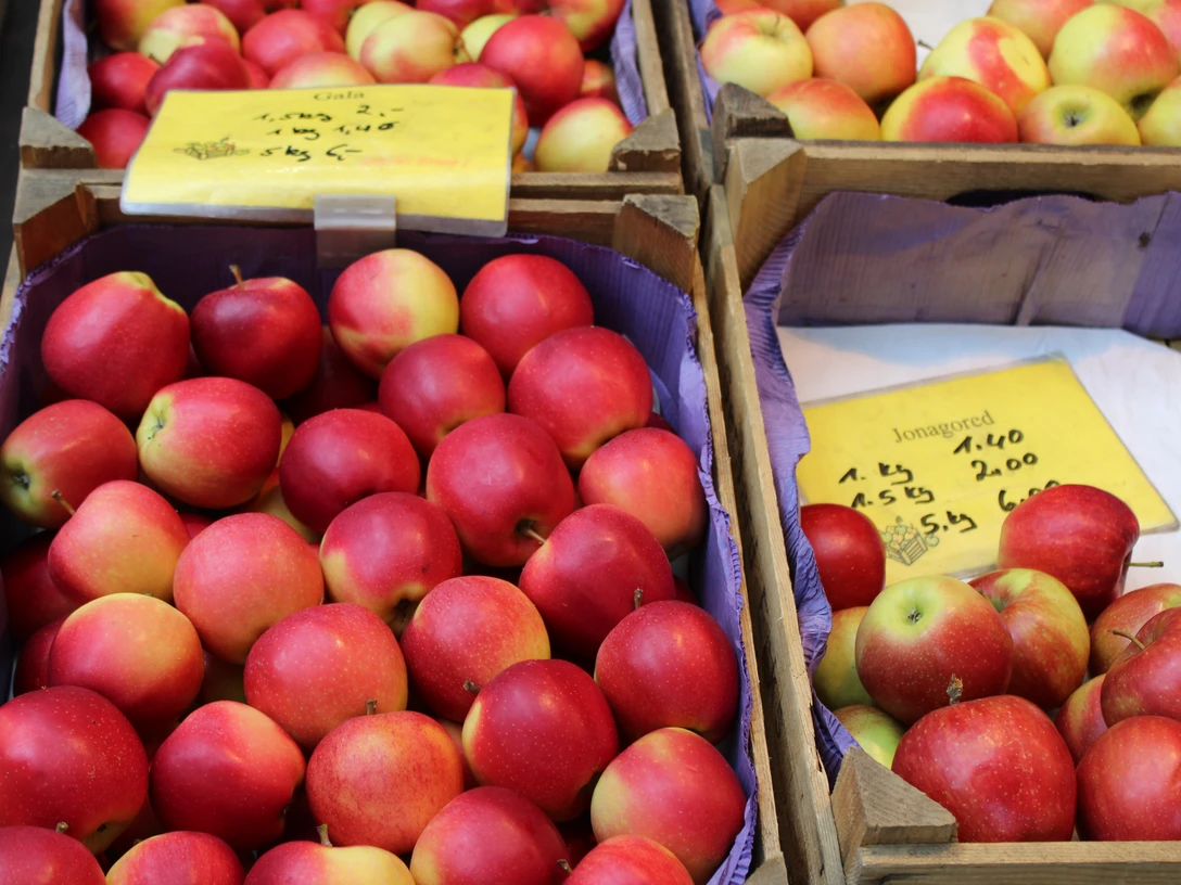 Reife, rote und gelbe Äpfel in Holzkisten auf einem Marktstand mit Preisetiketten darauf.