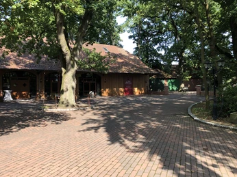 Roter Backsteinweg führt zu einem restaurierten Gebäude aus Holz mit rustikalen Fenstern unter Bäumen.A red brick path leads to a restored wooden building with rustic windows under trees.En rød murstenssti fører til en restaureret træbygning med rustikke vinduer under træer.Een pad van rode bakstenen leidt naar een gerestaureerd houten gebouw met rustieke ramen onder bomen.