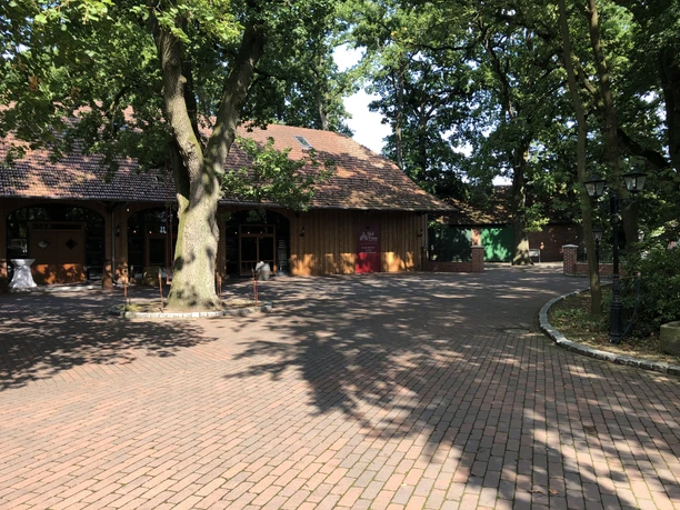 A red brick path leads to a restored wooden building with rustic windows under trees.