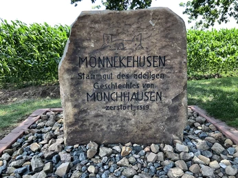Gedenkstein für das adlige Geschlecht von Münchhausen, umgeben von Kieselsteinen und grüner Vegetation.