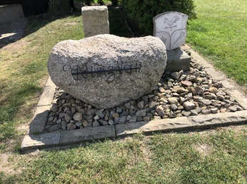 Ein großer Felsblock mit der Aufschrift "Windkraft" liegt auf einem mit Steinen umrandeten Platz.