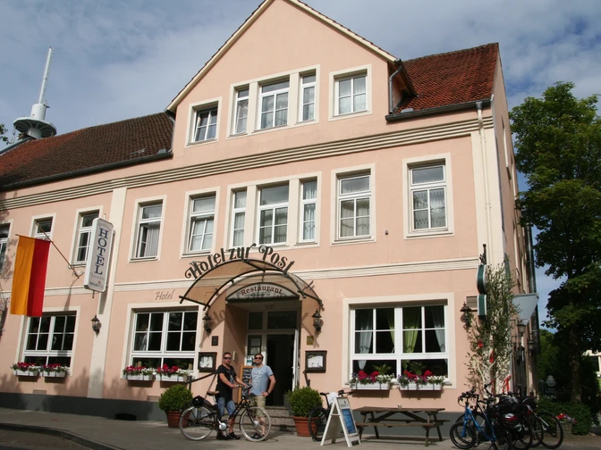 Hotelgebäude mit rosafarbener Fassade und weiß umrahmten Fenstern, vor dem Fahrräder stehen.