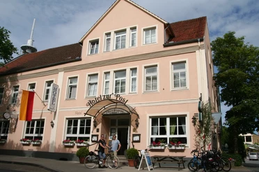 Hotel u. Restaurant zur Post Hotelgebäude mit rosafarbener Fassade und weiß umrahmten Fenstern, vor dem Fahrräder stehen.