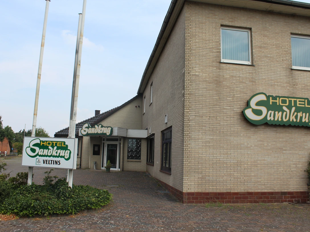 Hotel Sandkrug Ein großes Backsteingebäude des Hotel Sandkrug mit grünen Schildern und einem Kopfsteinpflasterweg.