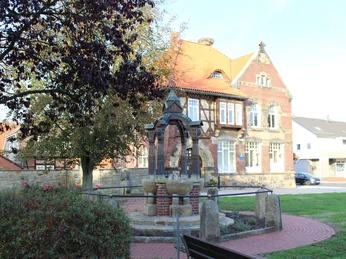 Ortsmitte Rehburg Historischer Brunnen in Rehburgs Ortsmitte, flankiert von Bäumen und einem stattlichen Fachwerkhaus.