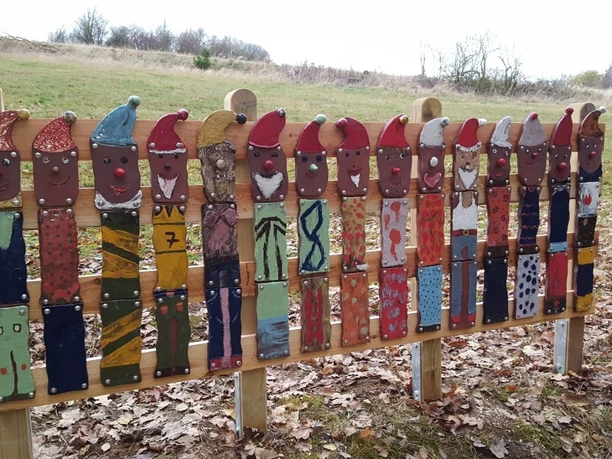 Skulpturen am Wegesrand Bleiwäsche Zwölf bemalte Holzlatten in Zwergenform stehen auf einem Laubboden in einer ländlichen Landschaft.