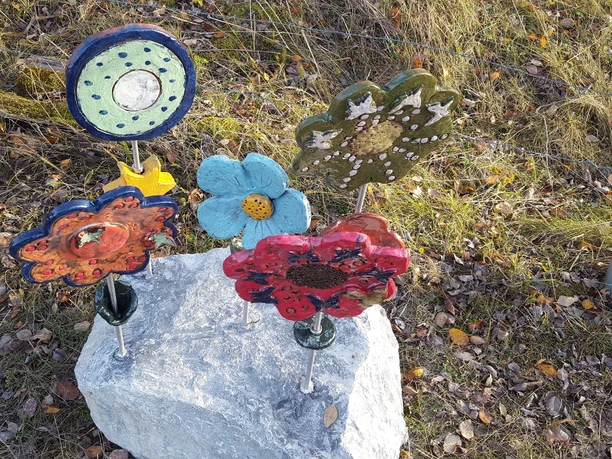 Skulpturen am Wegesrand Bleiwäsche Bunte Keramikblumen, kunstvoll gestaltet, stehen auf einem Stein inmitten von Gras und Laub.