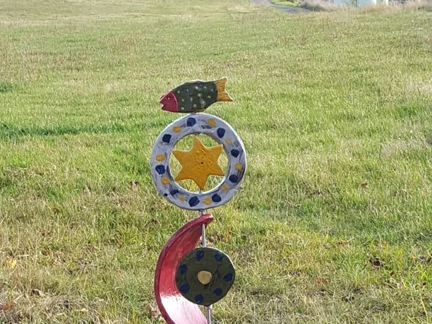 Skulpturen am Wegesrand Bleiwäsche Bunte Skulptur aus Metall auf einem Stein im Grünen, bestehend aus Mond-, Fisch- und Sternmotiven.