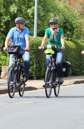 Radfahrer Drei Radfahrer und ein Kind in einem Fahrradanhänger fahren entspannt auf einer Wohnstraße entlang.