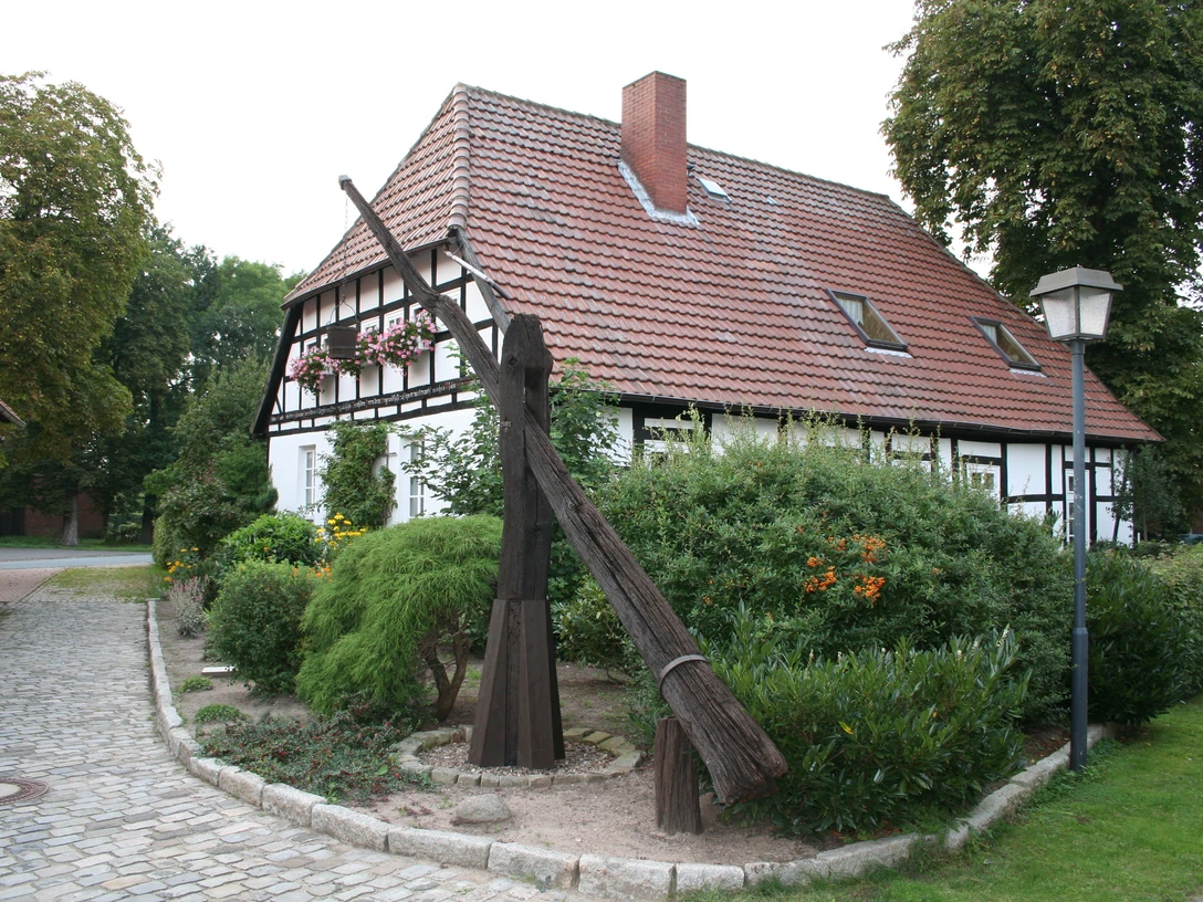 Ziehbrunnen Leese Ein historischer Ziehbrunnen steht vor einem Fachwerkhaus umgeben von Büschen und bunten Blumen.