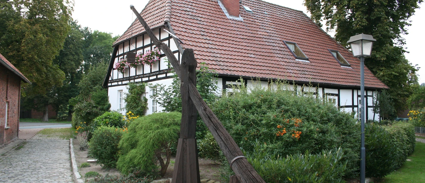 Ziehbrunnen Leese Ein historischer Ziehbrunnen steht vor einem Fachwerkhaus umgeben von Büschen und bunten Blumen.