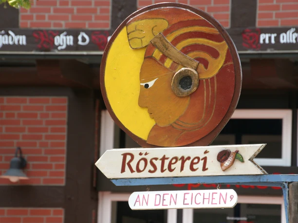 Round roastery sign with head in profile and coffee bean indicates a café in a half-timbered building.