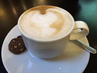 Kaffeetasse Cappuccino mit cremigem Milchschaum in der Tasse, auf einem weißen Unterteller mit Schokokeks.