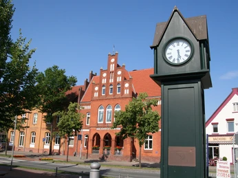 Historische Uhr in Stolzenau vor roten Backsteinfassaden an einem sonnigen Tag mit klarem Himmel.