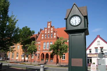 Normaluhr Stolzenau Historische Uhr in Stolzenau vor roten Backsteinfassaden an einem sonnigen Tag mit klarem Himmel.
