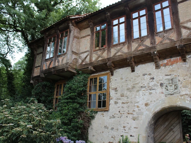 Fachwerkgebäude des Ritterguts Brokeloh mit Efeu. Steinwand mit Wappen, Holztüren und Sprossenfenster im Grünen.