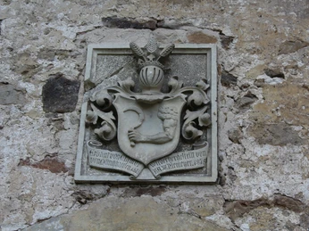 Wappen mit Helmzier aus Stein an einer historischen, verwitterten Wand, filigran und detailreich gestaltet.