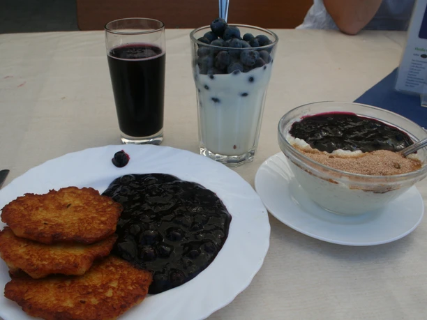 Three plates of blueberry pancakes, blueberry pudding and buttermilk with blueberries on a table.