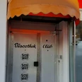Subway Silberne Edelstahltür unter einer gelben Markise, beschriftet mit "Discothek Club" und Subway-Logo.Silver stainless steel door under a yellow awning, labeled "Discothek Club" and Subway logo.