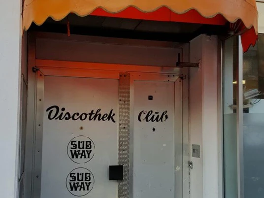 Subway Silberne Edelstahltür unter einer gelben Markise, beschriftet mit "Discothek Club" und Subway-Logo.Silver stainless steel door under a yellow awning, labeled "Discothek Club" and Subway logo.