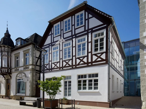 Zweistöckiges Fachwerkhaus mit weißen Fassaden und dunkelbraunen Holzbalken, seitlich Straße.