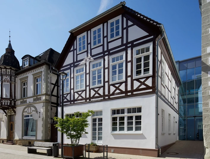 Zweistöckiges Fachwerkhaus mit weißen Fassaden und dunkelbraunen Holzbalken, seitlich Straße.