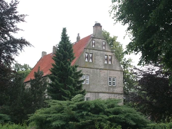 Schlüsselburg Backstein-Gebäude mit rotem Ziegeldach hinter dichtem grünen Laub im ländlichen Niedersachsen.