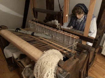 Ilser Webstube Eine traditionelle Webmaschine mit hölzernen Rahmen, Leinen und Puppe in historischer Kleidung.
