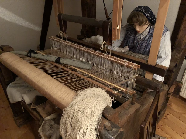 Ilser Webstube Eine traditionelle Webmaschine mit hölzernen Rahmen, Leinen und Puppe in historischer Kleidung.