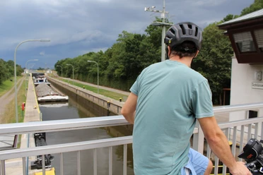Schleuse Schlüsselburg Ein Radfahrer beobachtet von einer Brücke aus ein vorbeifahrendes Schiff in der Schleuse Schlüsselburg.