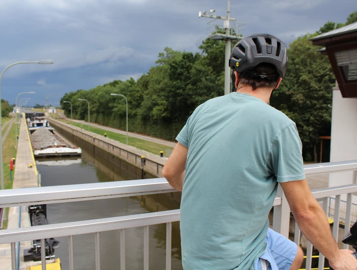 Schleuse Schlüsselburg Ein Radfahrer beobachtet von einer Brücke aus ein vorbeifahrendes Schiff in der Schleuse Schlüsselburg.