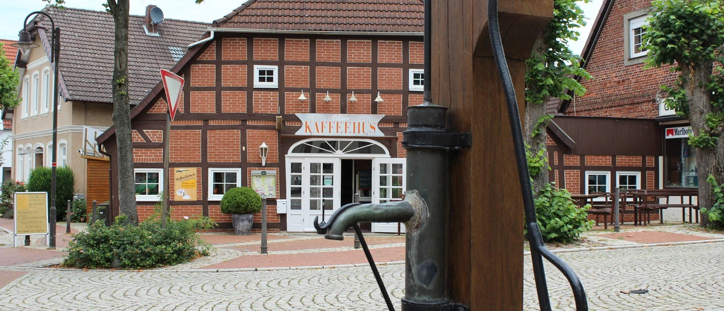 Historisches Fachwerkhaus mit Café im Zentrum von Bruchhausen-Vilsen und alter Wasserpumpe im Vordergrund.