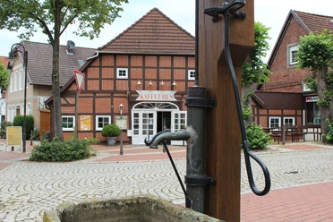 Ortsmitte Bruchhausen-Vilsen Historisches Fachwerkhaus mit Café im Zentrum von Bruchhausen-Vilsen und alter Wasserpumpe im Vordergrund.