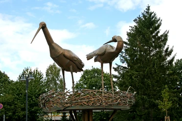Störche im Kreisel Zwei metallene Storchfiguren stehen auf einem kunstvoll gestalteten Nest inmitten eines Kreisverkehrs.